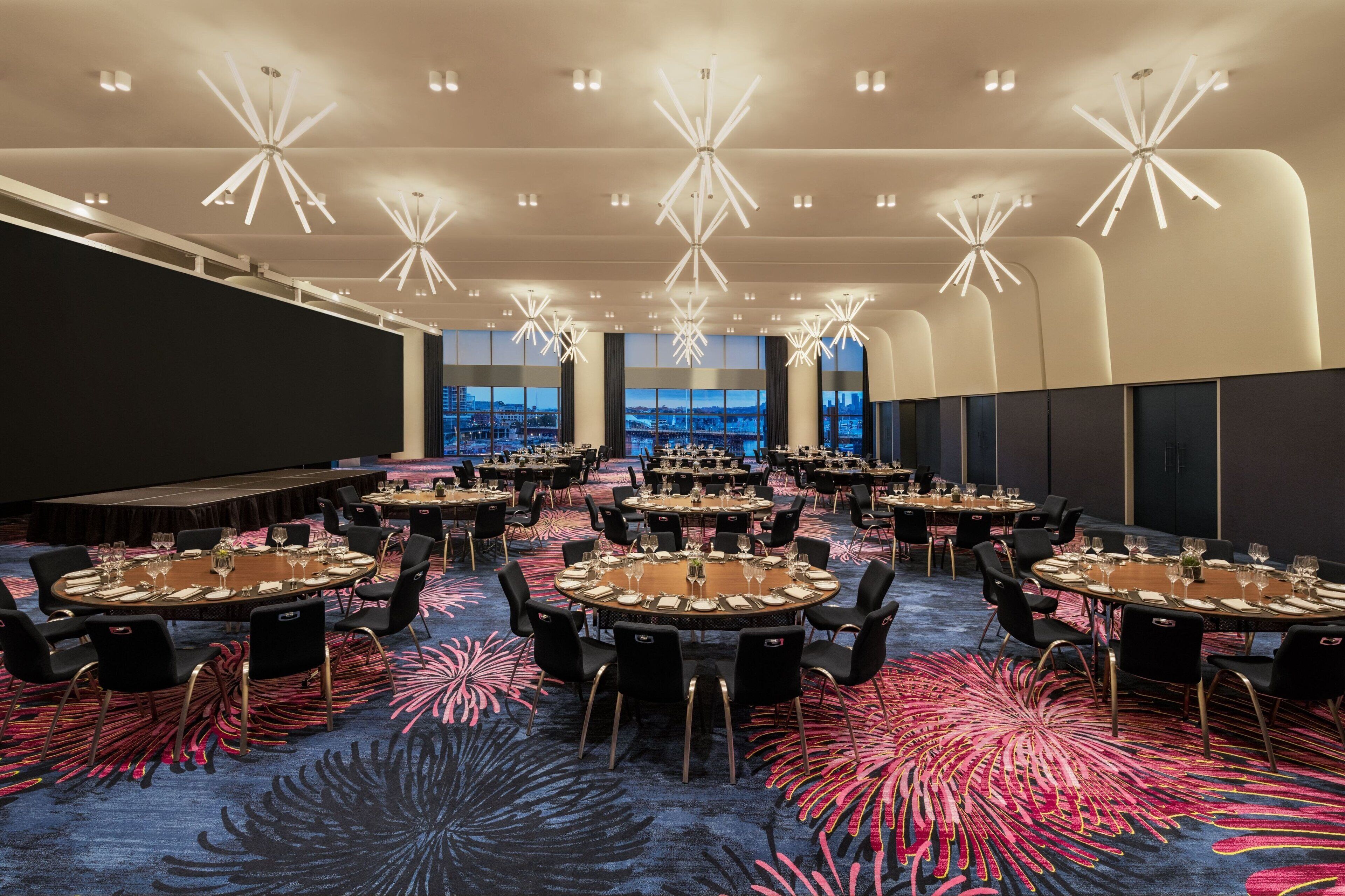 A conference room with multiple round tables, black chairs, and a carpet with a floral pattern.