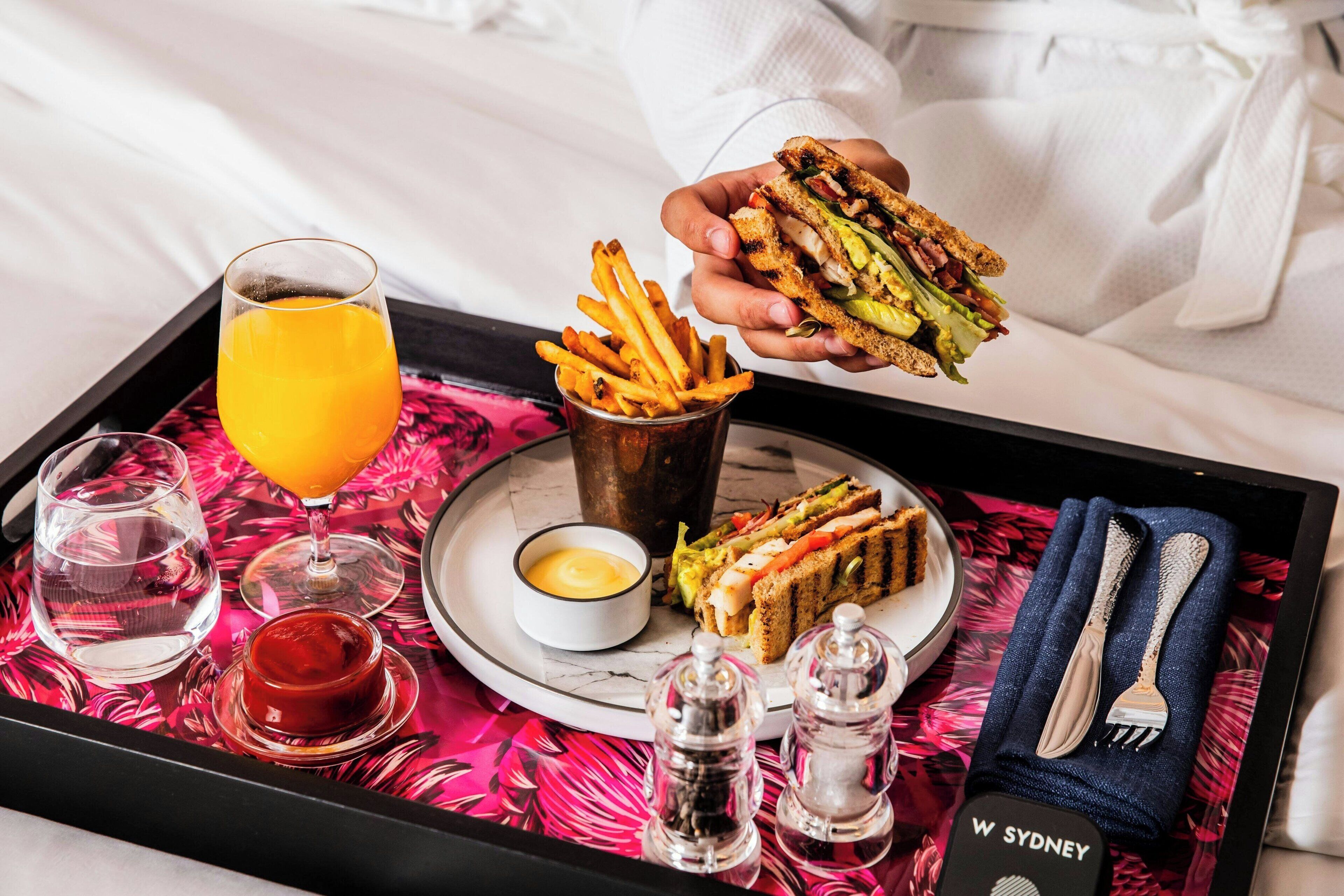 Ein Tablett mit einem Sandwich, Pommes Frites, einem Glas Orangensaft, einer kleinen Schale Sauce und Beilagen.