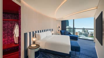 A modern hotel room with a large bed, a seating area, a wardrobe, and a city view.