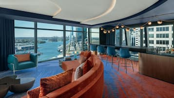 Una habitación de hotel moderna con un sofá curvo, una zona de bar y ventanas amplias con vistas a la ciudad.