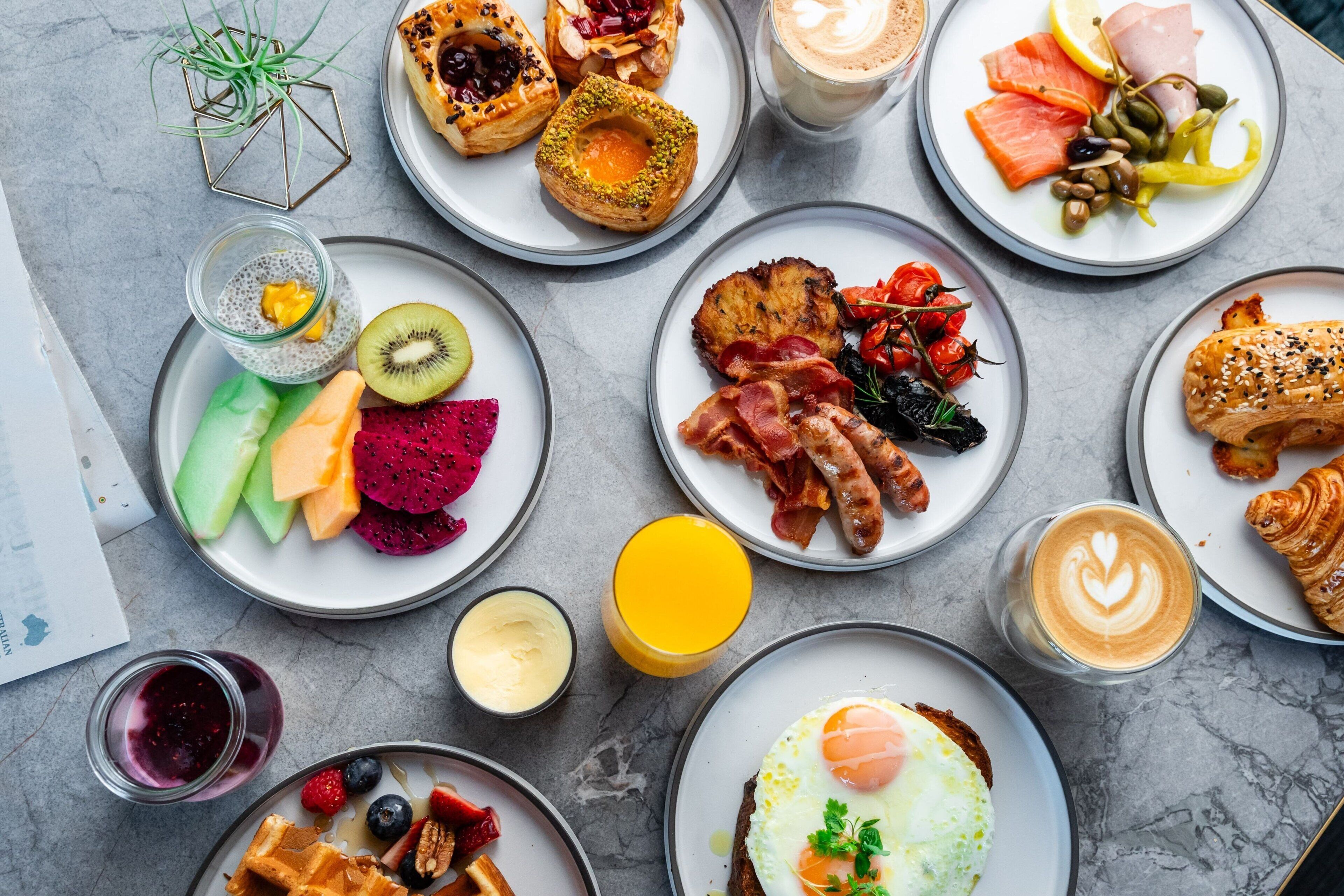 A variety of breakfast dishes including pancakes, eggs, bacon, and pastries on plates.