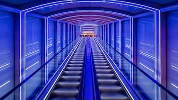 An escalator in a modern, brightly lit corridor with geometric patterns on the walls.