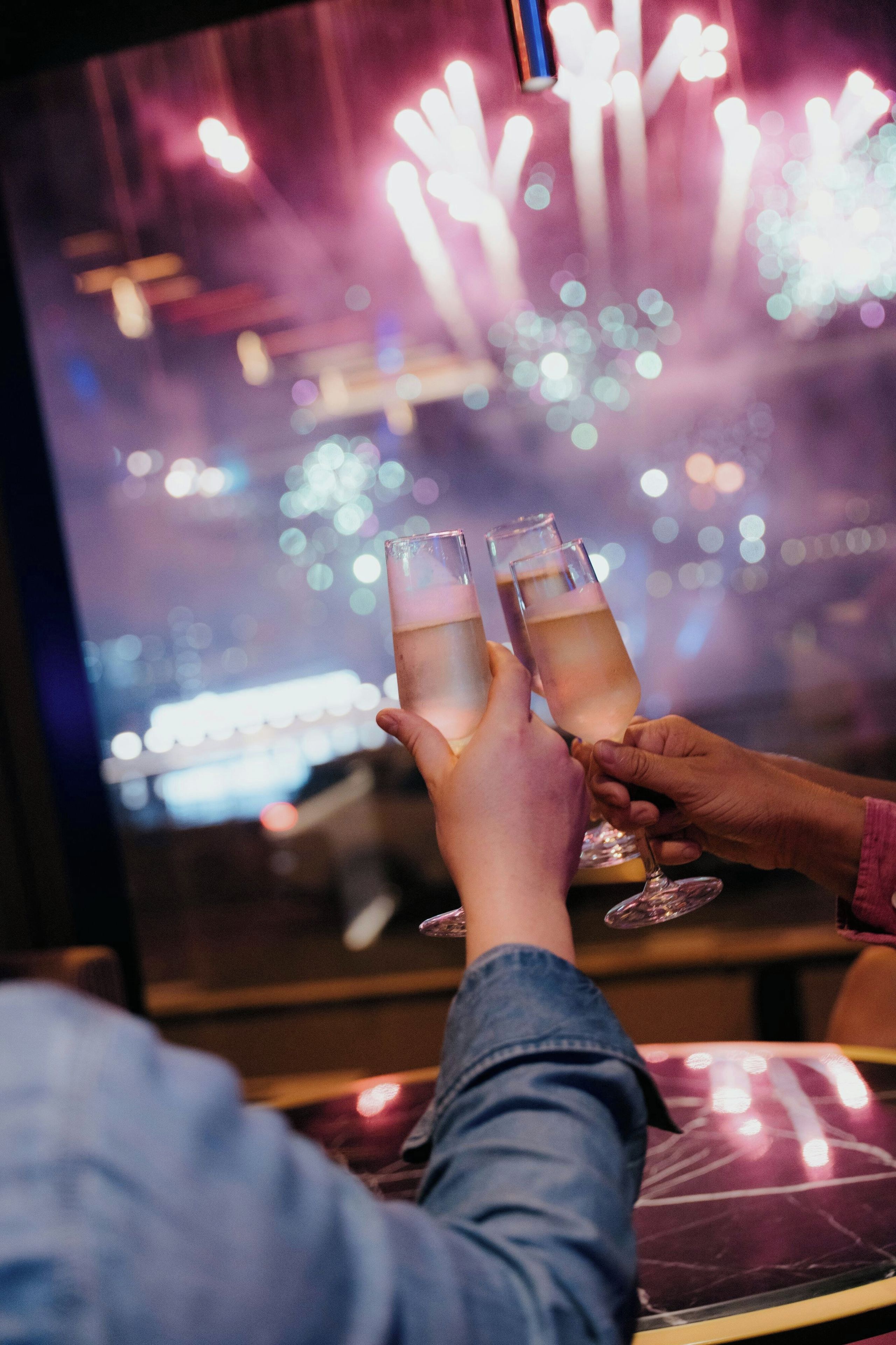 Two hands holding glasses with a beverage, with a blurred background of lights.