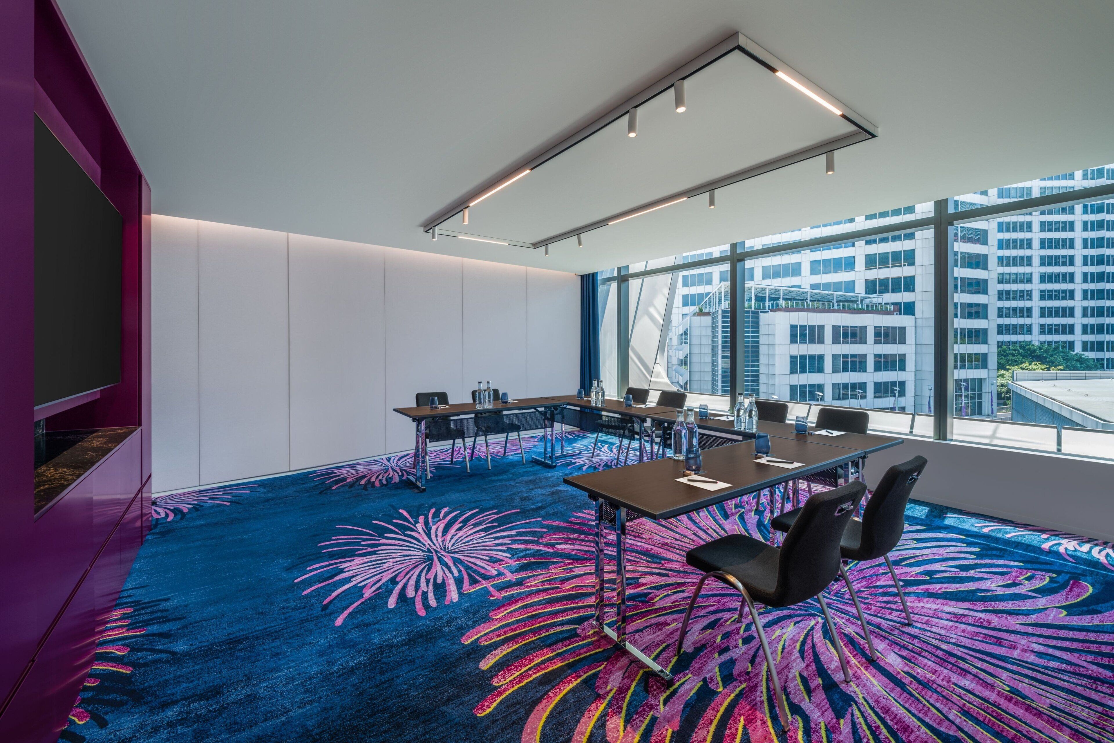 A conference room with a large table, chairs, and a vibrant carpet.