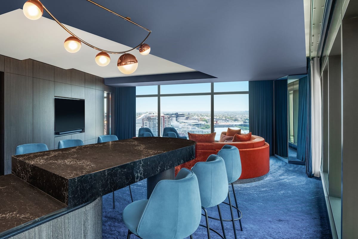 A modern bar area with a large marble countertop, blue chairs, and a seating area with orange sofas.