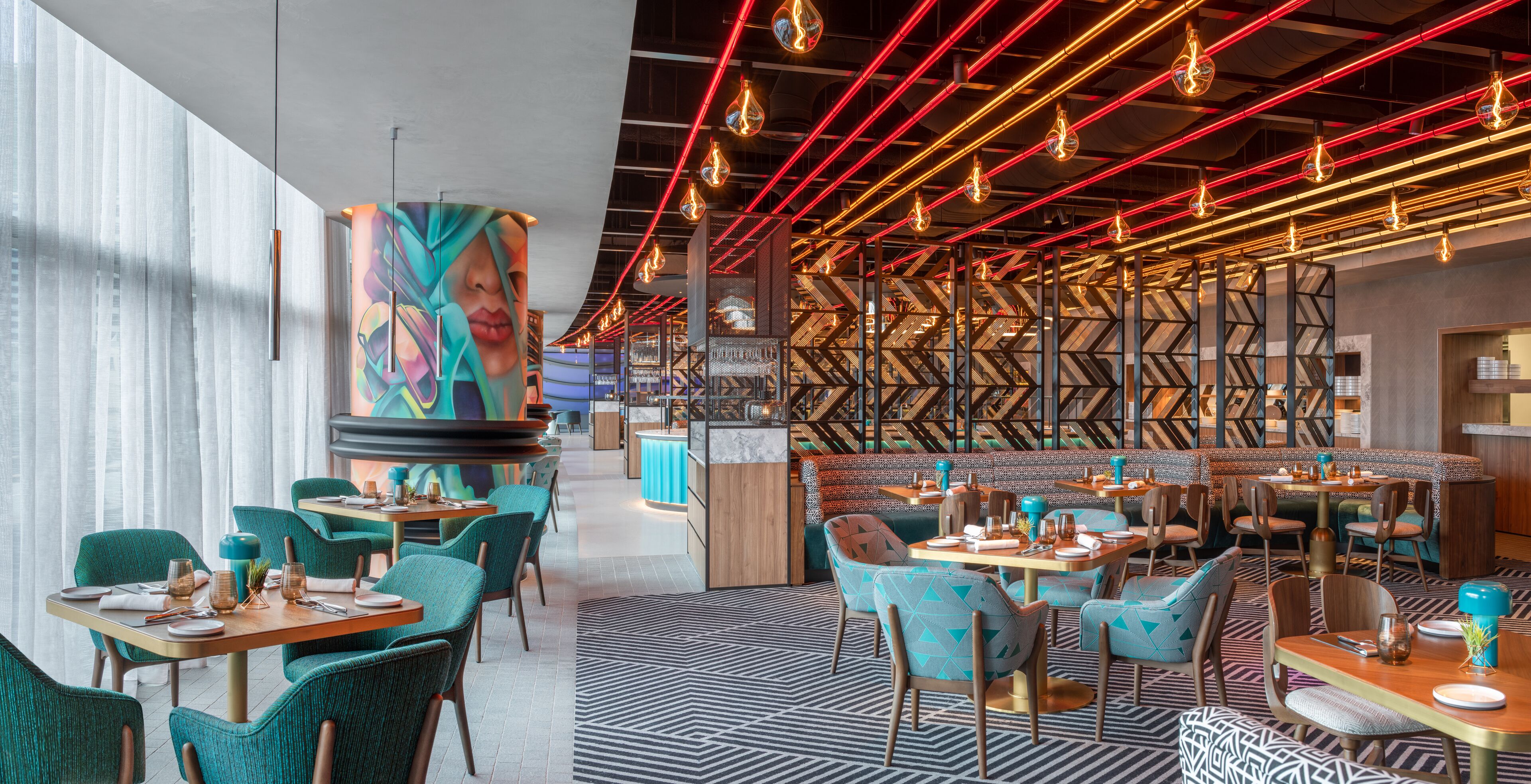 A modern restaurant interior with teal chairs, wooden tables, and a patterned floor.