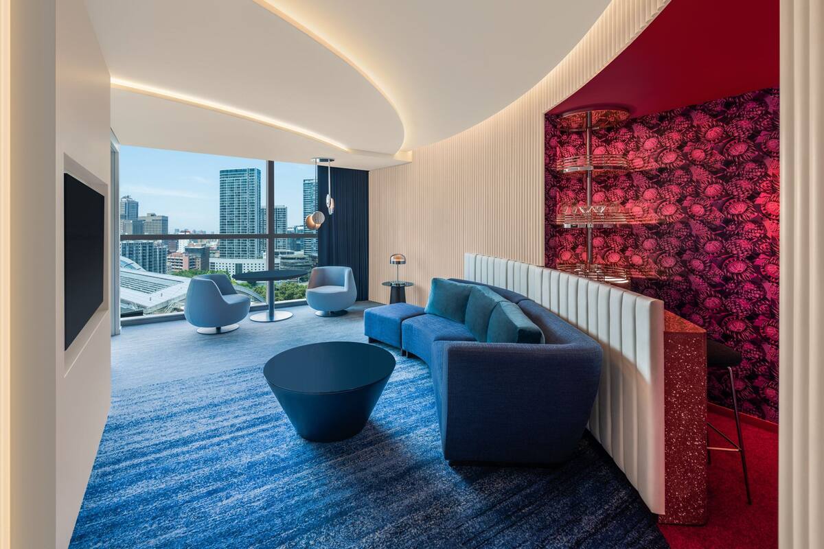 A modern living room with a blue carpet, a sofa, a coffee table, and a city view through large windows.