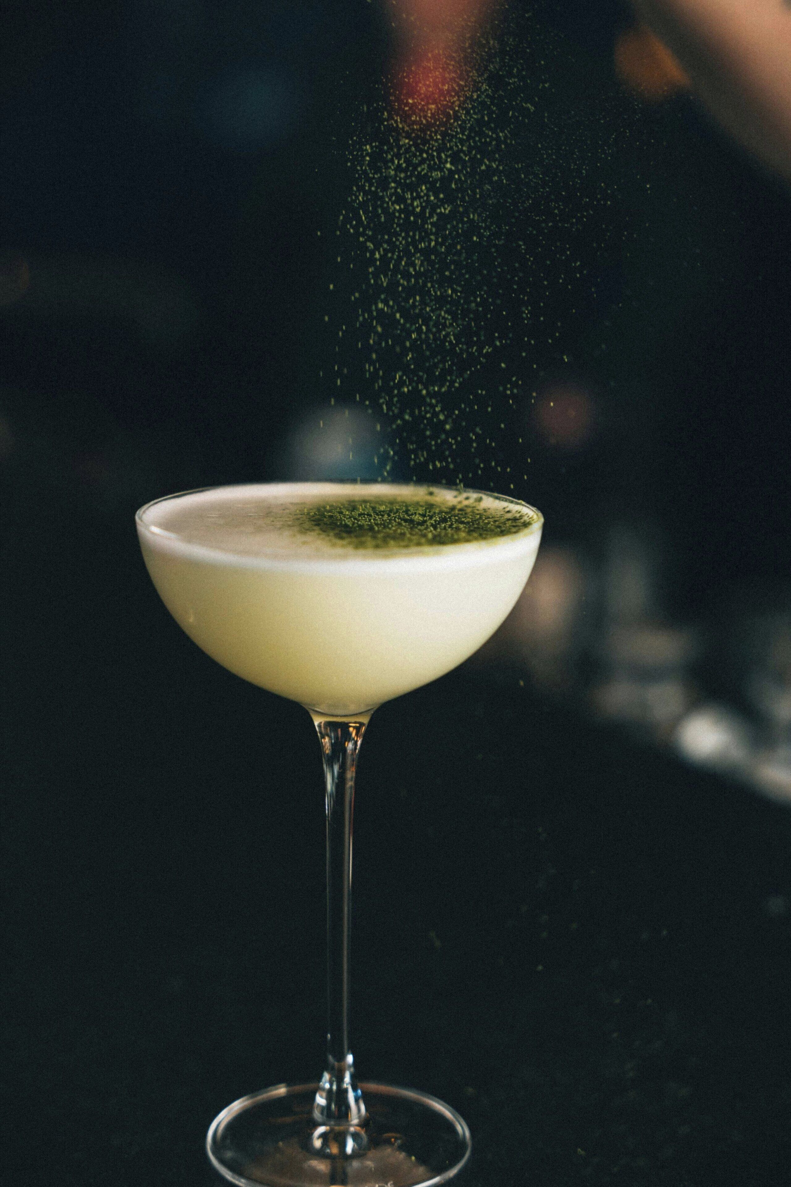 Un verre à martini orné d’une garniture verte, posé sur une surface sombre.