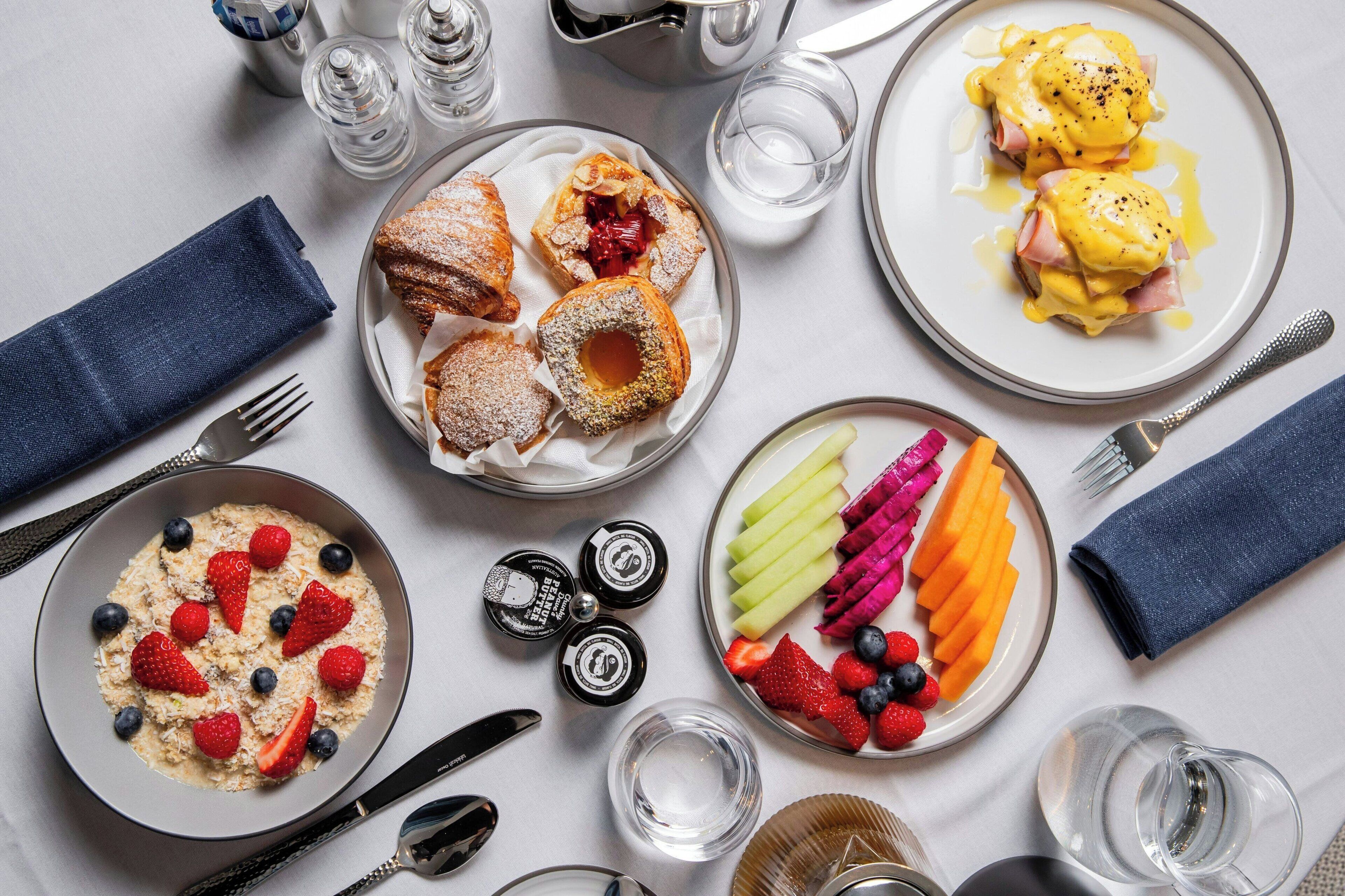 A breakfast table with various dishes including eggs Benedict, pastries, and a fruit platter.