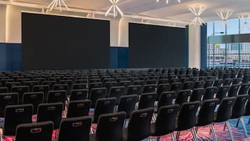 A large indoor auditorium with rows of black chairs and large screens.