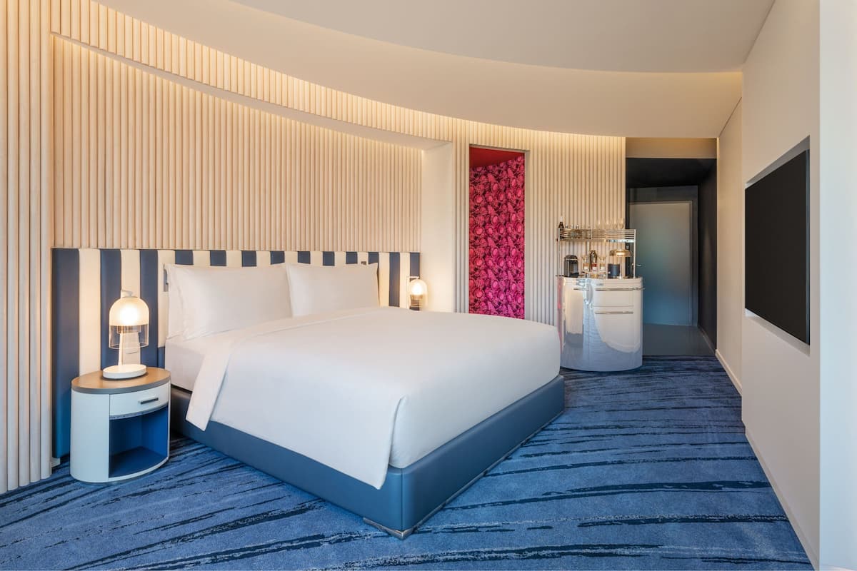 A modern hotel room with a large bed, bedside tables, a vanity with a mirror, and a wardrobe.