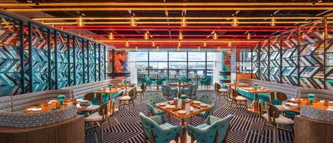Un restaurante moderno con diseños geométricos en las paredes, techos a la vista y diferentes opciones de asientos, como mesas y cabinas.