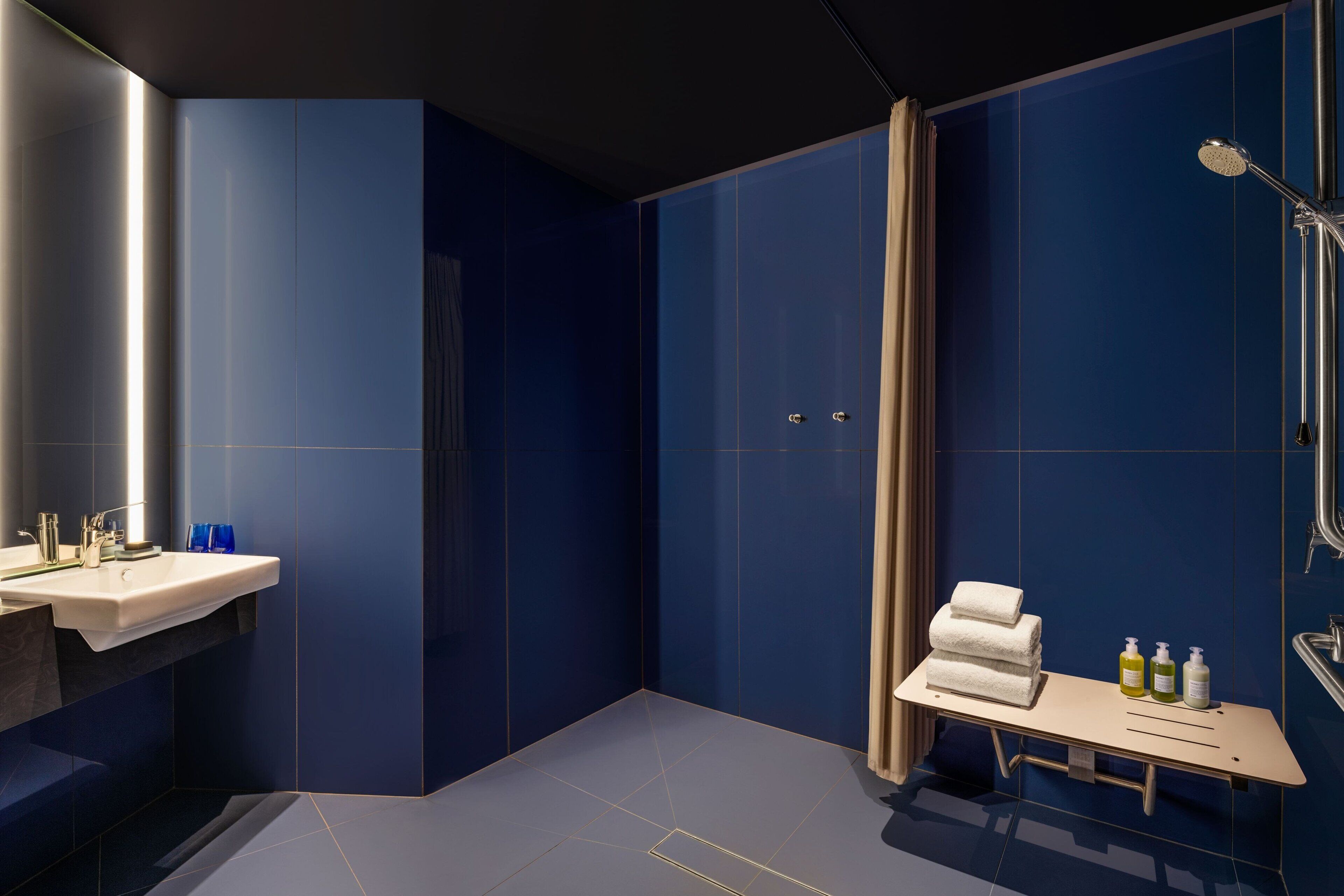 Un baño moderno con un espejo grande, un lavabo, una ducha y una tocador con artículos de aseo.