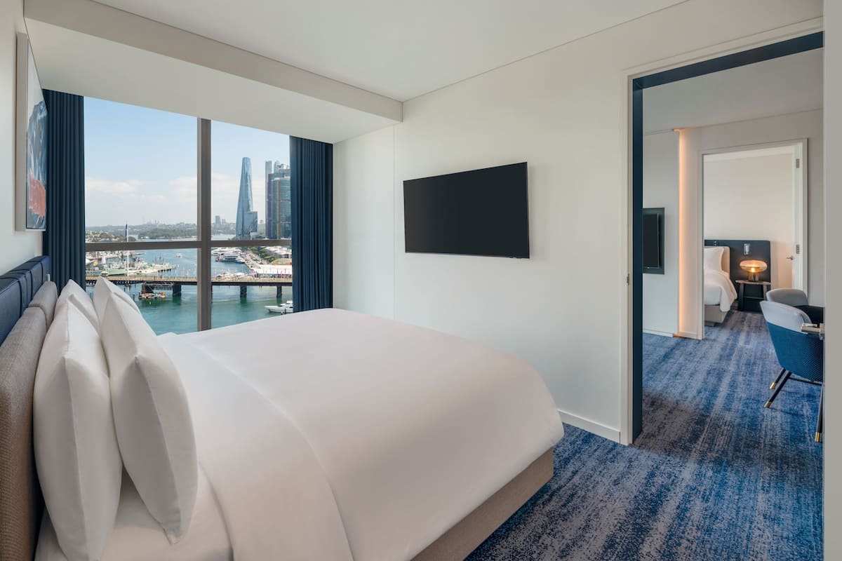 A hotel room with a large bed, a TV mounted on the wall, and a view of a cityscape through a large window.