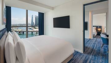 A hotel room with a large bed, a TV mounted on the wall, and a view of a cityscape through a large window.