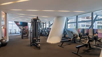 A modern gym with various exercise equipment, large windows, and a unique architectural design.