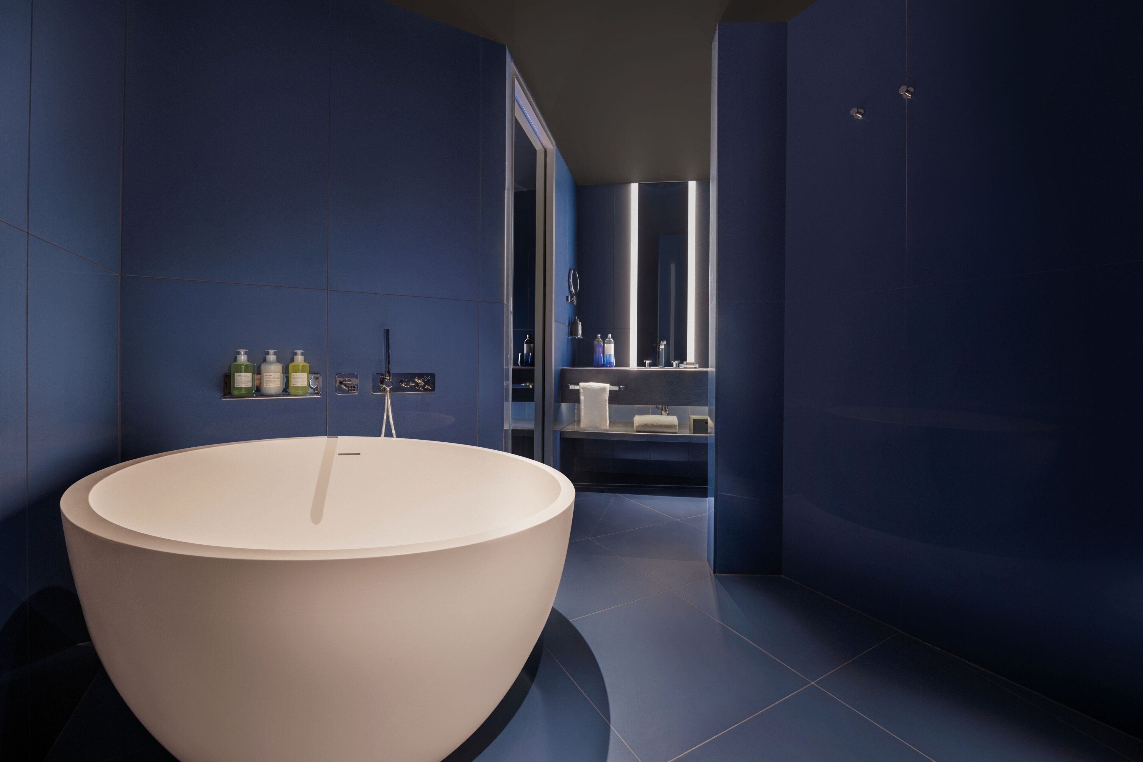 Un baño moderno con una bañera independiente grande, un espejo y un estante con artículos de aseo.