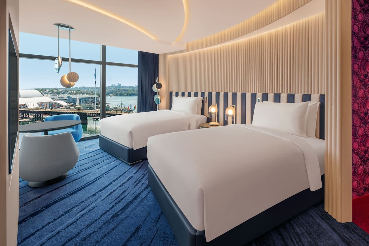 A hotel room with two beds, a view of the city, and a balcony with a table and chairs.