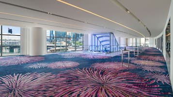 Un hall d’hôtel spacieux, agrémenté d’un grand tapis aux couleurs vives, d’un escalier moderne et de grandes fenêtres offrant une vue sur la ville.