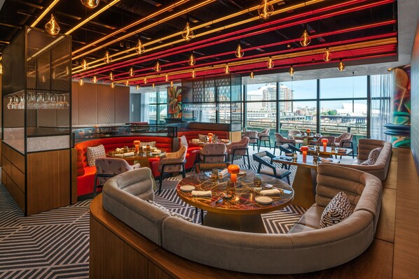 A modern lounge area with a curved sofa, round tables, and a city view through large windows. - W Sydney (Sydney)