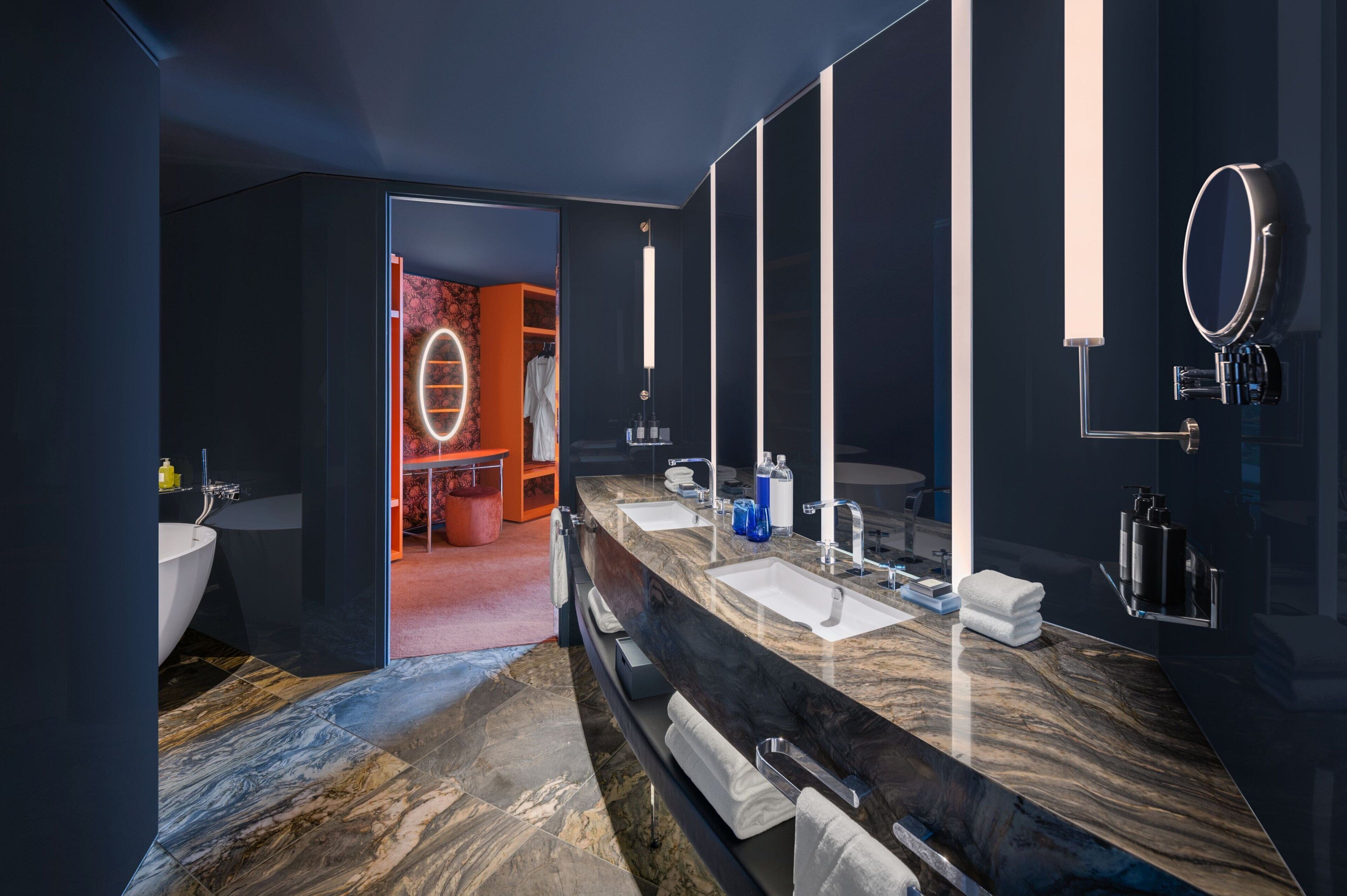 A modern bathroom with a dark color scheme, two sinks, a large mirror, and a vanity area.