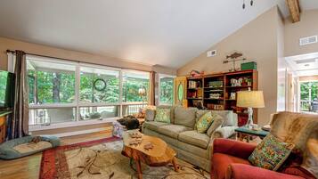 Un salon chaleureux avec une grande fenêtre, un canapé, un fauteuil rouge et une table basse en bois.