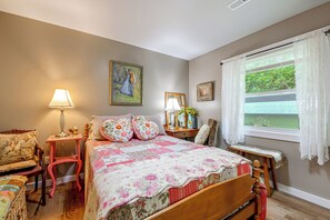 Une chambre à coucher avec un lit, une chaise, une table de chevet, une lampe et une fenêtre avec des rideaux.