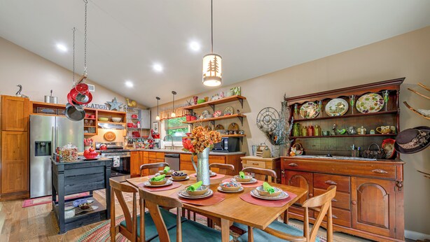 Una cocina con armarios de madera, una mesa de comedor preparada para cuatro personas y una variedad de utensilios de cocina en estantes.