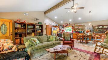 Un salon spacieux avec un canapé vert, une table basse en bois et un coin repas comprenant une chaise rouge et une table en bois.