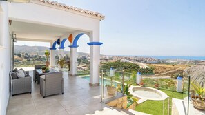 Un'area esterna riparata con posti a sedere, una piscina e vista sul paesaggio costiero.