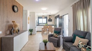 A modern living room with a sofa, coffee table, and decorative items. There is a dining area with a table and chairs, and a kitchen in the background. - Casa Mirador Azul Torrox by Ruralidays (Málaga)