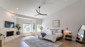 Ein geräumiges Schlafzimmer mit einem großen Bett, einem Deckenventilator, einem Kamin und Blick ins Freie.
