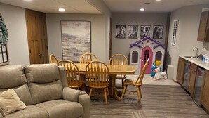 A living room with a beige sofa, wooden dining table, and chairs. There is a playhouse with a pink door and a blue horse figure. - 2027 Oshkosh EAA rental — 4.5 miles from the AirVenture (Oshkosh)