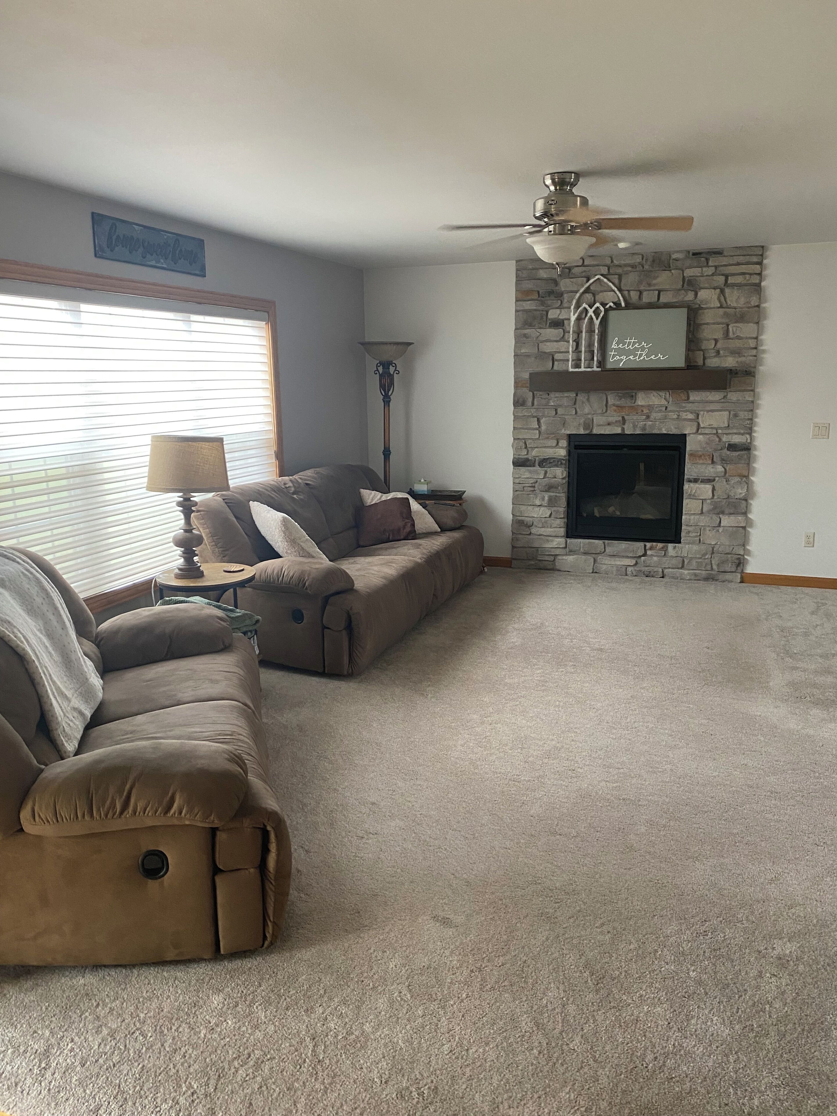 A living room with a stone fireplace, a ceiling fan, and a sofa set.