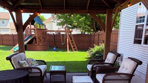 A covered patio with wicker furniture, a small table, and a swing set in the background. - 2027 Oshkosh EAA rental — 4.5 miles from the AirVenture (Oshkosh)
