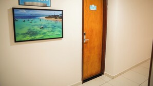 Ein Flur mit einem Schild, das die Zimmernummern 301 bis 307 anzeigt, einer Tür mit der Aufschrift 'Apt. 301' und einem gerahmten Bild mit einer Strandansicht.