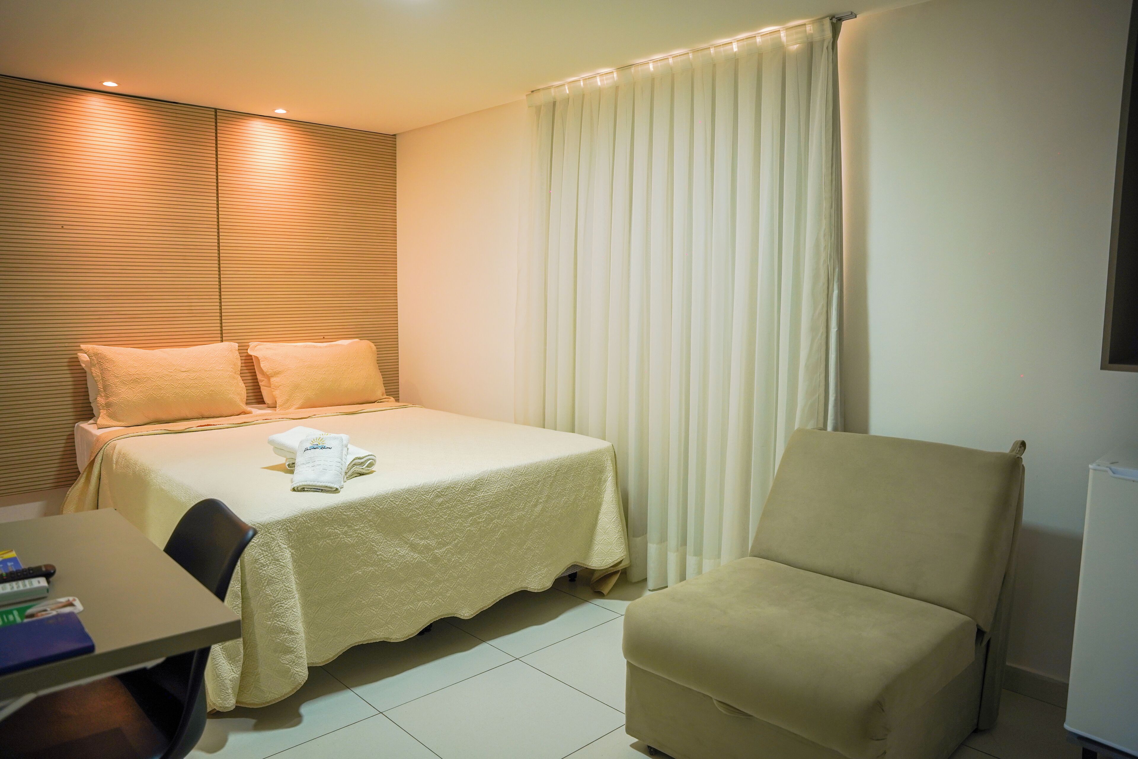 A hotel room with a bed, a chair, a table, and a window with curtains.