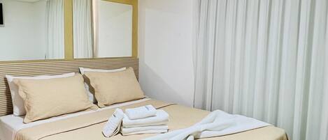 Une chambre d’hôtel avec un grand lit, un téléviseur à écran plat, une table de chevet et une fenêtre avec des rideaux.