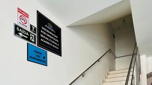 Eine Treppe mit Metallgeländer und weißen Stufen. An der Wand befinden sich Schilder, die Rauchen und Müll verbieten sowie Zugang zu Apartments anzeigen.