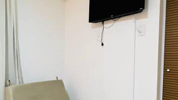A small room with a bed, a flat-screen TV mounted on the wall, and a wooden door.