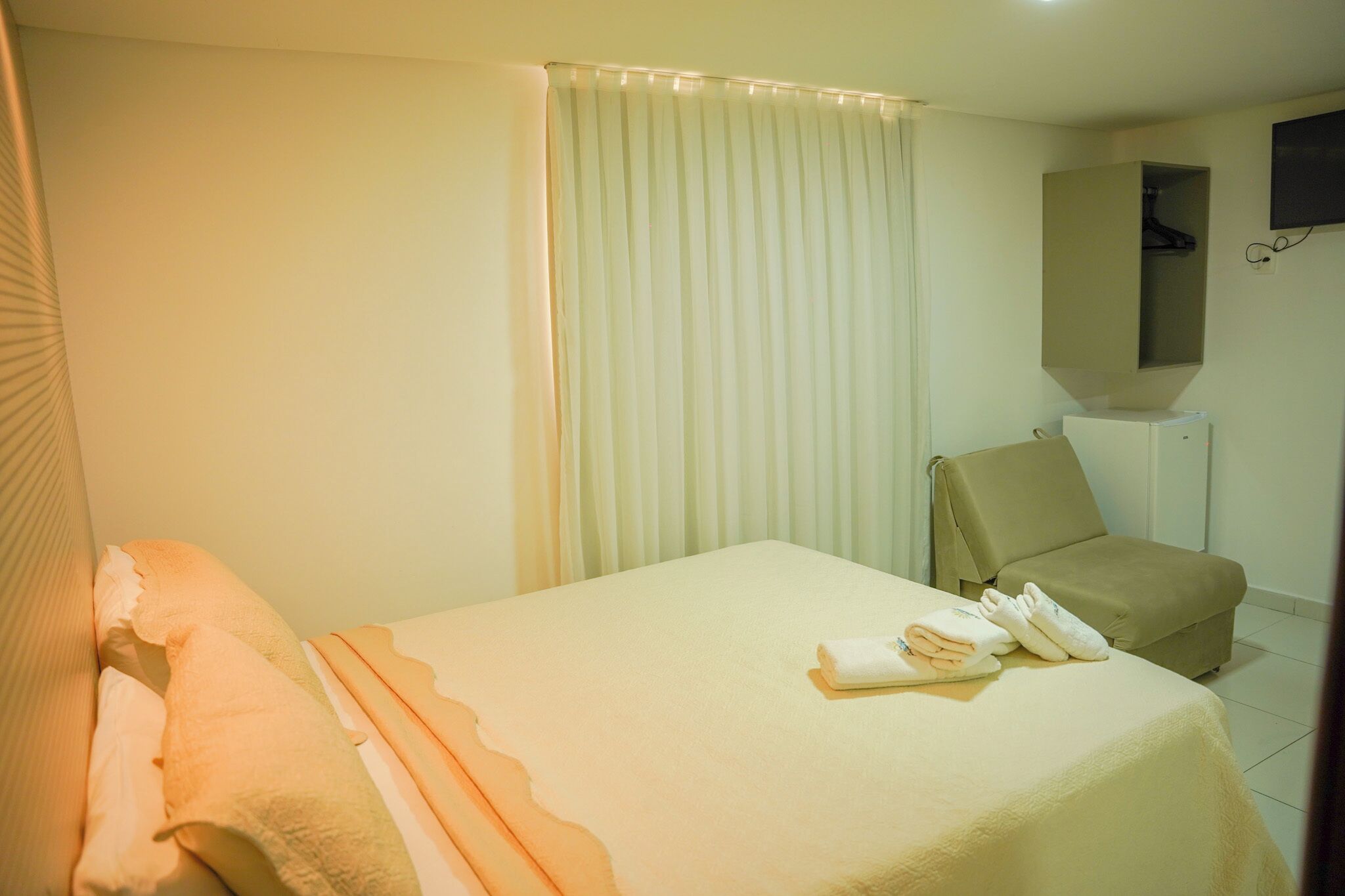 A hotel room with a bed, a chair, a mirror, and a television.