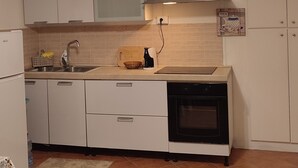 Een kleine keuken met witte kastjes, een roestvrijstalen spoelbak, een inbouwoven en een hangende lamp.