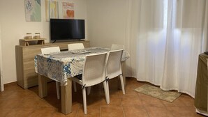 Een eethoek met een tafel voor vier personen, een televisie op een standaard en kunst aan de muur.