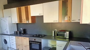 A compact kitchen with a washing machine, a stove, a microwave, and a sink. - Maison Proche Centre Ville de Moulins (Yzeure)