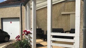 A covered outdoor seating area with a white railing, a garage door, and a car parked nearby. - Maison Proche Centre Ville de Moulins (Yzeure)