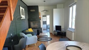 A modern living room with a fireplace, a dining area, and a TV. - Maison Proche Centre Ville de Moulins (Yzeure)