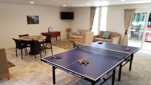 Une table de ping-pong dans un salon, avec un canapé, un téléviseur et un coin repas.