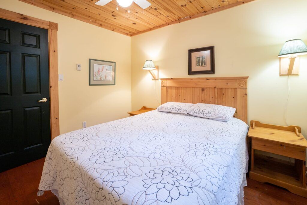 Una camera da letto con una testiera in legno, una coperta con motivi floreali, due lampade ai comodini e un quadro appeso al muro.