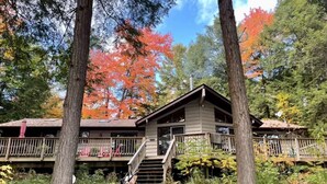Una baita con una veranda in legno, una scala che conduce all'ingresso principale e una foresta circostante con foglie autunnali.