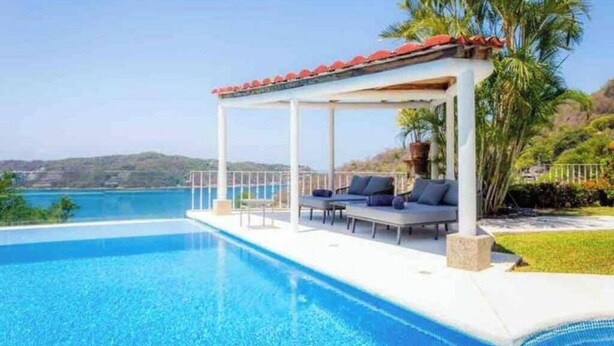 A poolside area with a covered seating area, a clear view of the water, and a mountainous landscape in the background. - ESPECTACULAR CASA EN ACAPULCO (Laredo)